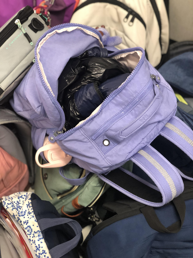 A backpack stuffed with a coat, a pencil pouch, several notebooks and folders, along with other school supplies.