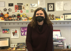 English teacher Ms. Balduf by her desk and shelves, with fictional character merchandise, inside her classroom.